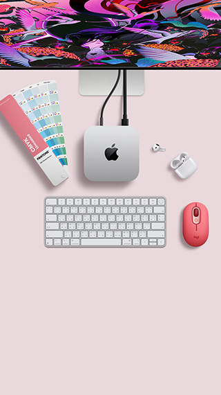 Mac mini, ด้านบน, อะลูมิเนียมสีเงิน, มุมมน, โลโก้ Apple สีดำมันเงาอยู่ตรงกลาง, เชื่อมต่อด้วยสาย, มองเห็น Studio Display ที่ตั้งอยู่ด้านบนบางส่วน, AirPod 4, เปิดฝาอยู่, ตัวเลือกสี Pantone, คีย์บอร์ดและเมาส์ Logitech สีแดง