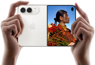 iPhone Duo, สีสตาร์ไวท์, ถืออยู่ในมือสองข้างในแนวนอน, กางเปิดอยู่, แผงด้านซ้ายแสดงกล้องหลัง Dual Fusion 48MP, แผงด้านขวาแสดงบุคคลหนึ่งขณะถ่ายภาพบนจอภาพภายนอก, ตัวแบบในภาพสามารถเห็นใบหน้าของตัวเองระหว่างกำลังถ่ายภาพโดยใช้ Duo Preview