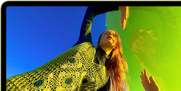 MacBook Neo, สีซิตรัส, หน้าจอแสดงภาพบุคคลที่กำลังยิ้มแย้มและนอนอยู่ในทุ่งดอกไม้ที่มีแดดจ้า