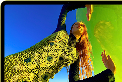 MacBook Neo, สีซิตรัส, หน้าจอแสดงภาพบุคคลที่กำลังยิ้มแย้มและนอนอยู่ในทุ่งดอกไม้ที่มีแดดจ้า